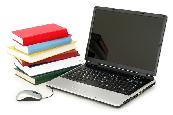 Laptop next to a pile of books.