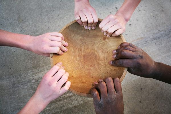 Wooden bowl being held by three sets of hands.