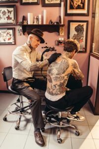 Picture of a tattoo artist tattooing the arm of a person who has a full back tattoo
